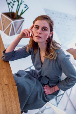 The girl poses in a cafe. The model is wearing a gray suit. Freckles on the girl's face. A fair-haired girl poses in a lit room near a lampの写真素材