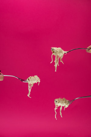 Pasta wrapped with a fork in a hand on a pink background. A female hand holds a fork with pasta. Three forks with spaghetti on the background, side view.の写真素材