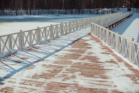 Snow-covered white wooden bridge across the river in winter. The bridge is painted white. Low pedestrian bridge in the park. Winter landscapeの写真素材