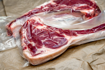 Raw lamb chops in plastic bag on brown paper background, top view