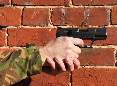 A 9mm Pistol being fired with  ejected case in the air this is against a brick wall
with just the hand and some sleeve showing with room for textの写真素材