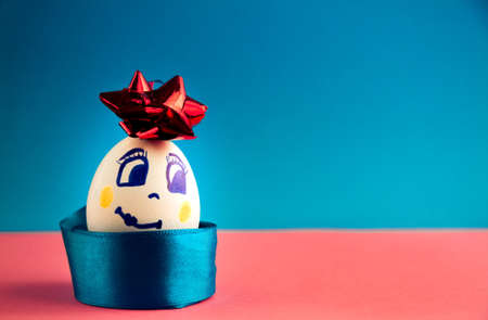 white. beautiful smiling egg with bow on pink and blue background, close-up.の写真素材
