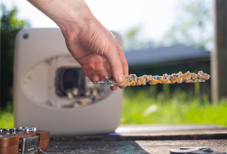 A man holding a anode damaged from corrosion. In the background the boiler with instruments and a view of the lawn. Close upの素材 [FY310124181444]