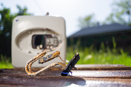 The water heating element damaged from corrosion lies on a wooden table next to the boiler. In the background green grass in the yard. Copy space.の写真素材