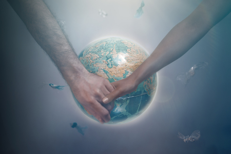 A man and a woman of different races holding hands on the background of the globe of the planet...