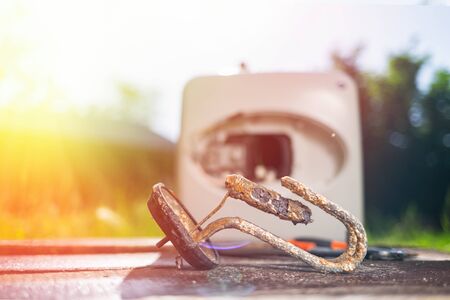 The water heating element damaged from corrosion lies with instrumets on a wooden table next to the boiler. In the background green grass in the yard. Copy space. Light.の写真素材