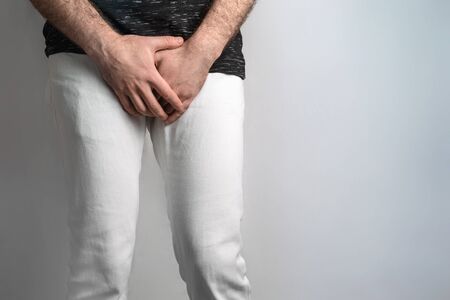 A man dressed in white jeans, holding hands on genitals. Disease for men. The concept of protection...