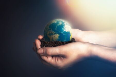 Womens hands holding soil with a globe of the planet Earth.The concept of environmental conservation, organic agriculture. Light from the topの写真素材