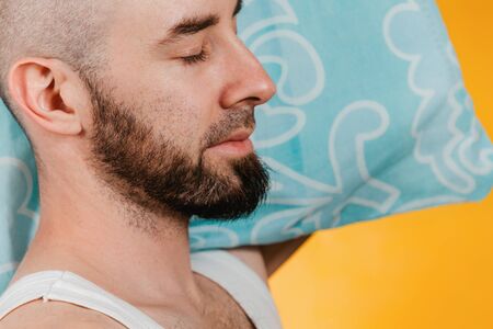 The concept of rest. A man quietly sleeping on blue pillow. Orange background. Close up.の写真素材