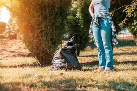 The concept of environmental pollution and Earth day. A woman volunteer removes garbage in the Park, near the feet is a black garbage bag. Copy space.の写真素材