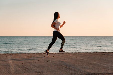Sports and Jogging along the sea. A young brunette woman runs along a path along the sea. In the...