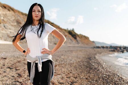 Concept of sport and healthy lifestyle. A young woman in sportswear, posing on a rocky beach,...