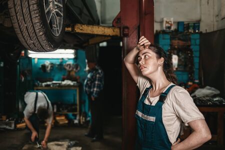 The concept of small business, feminism and women's equality. A young female auto mechanic wearily wipes sweat from her forehead.の写真素材