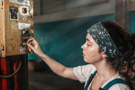 The concept of small business, feminism and women's equality. A young tired woman presses a button on the factory working mechanism.の写真素材