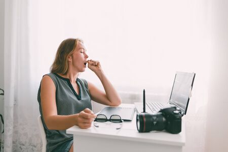 A young woman yawns in the workplace. Fatigue and overload in office work. Copy space.
