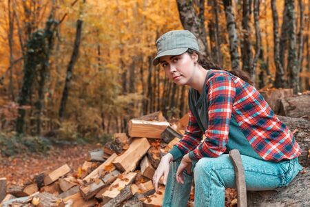 Preparation for the heating season. A pretty young woman sits on a log with an axe at her feet. In...