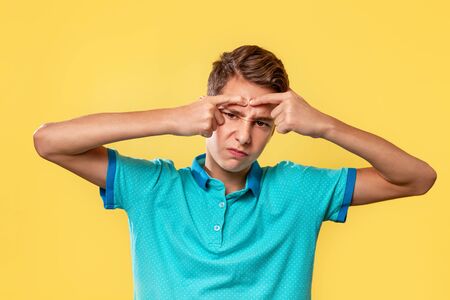 Cosmetology, Dermatology and acne. Caucasian teenager in a blue t-shirt, painfully squeezes out a pimple on his forehead. Yellow background. Copy space.の写真素材