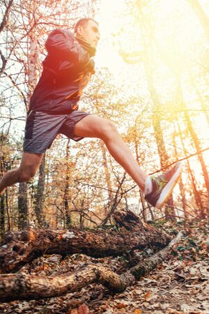 The concept of sports and cross-country running. A man in sportswear jumping branches on the ground,...