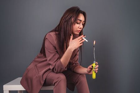 The concept of nicotine addiction. Caucasian young woman in a business suit, sitting on a stool and...