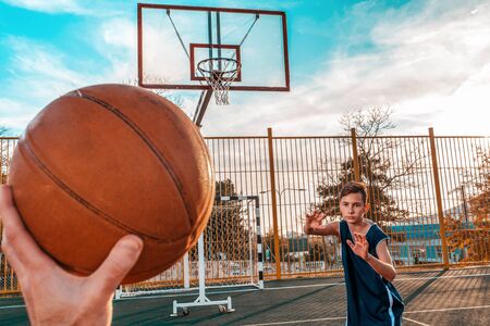 Sports and basketball. A mans hand holds a basketball for submission. In the background, a teenager preparing to catch a ball. Close upの写真素材