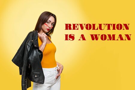 The concept of equal rights and feminism. An isolated shot of a Caucasian woman with makeup, who is holding a leather jacket. Yellow background. Revolution is a woman.の写真素材