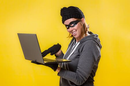 The concept of cybercrime and hacking. Portrait of a woman in a black hat, gloves and mask holding a...