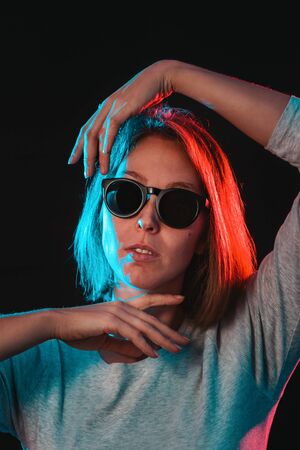 The neon lights of the club. Portrait of a young woman in glasses, posing with her hands. Side blue...