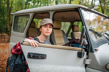 A young Caucasian woman with a backpack climbs into a jeep. In the background, trees and forest....