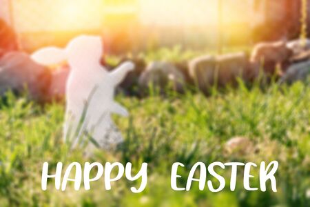 The concept of Easter holidays. Decorative handmade craft in the form of a rabbit, located next to the painted egg. Green grass in the background. Light and inscription "Happy Easter".の写真素材