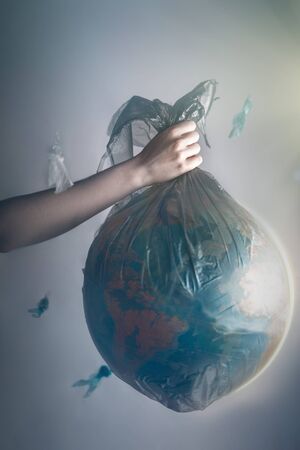 A woman's hand holding a garbage bag with a globe of planet Earth.Concept of environmental pollution and earth day. Tint.の写真素材