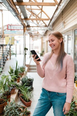 Internet and mobile phone. Young pretty blonde woman uses smartphone. In the background, a city street.の写真素材
