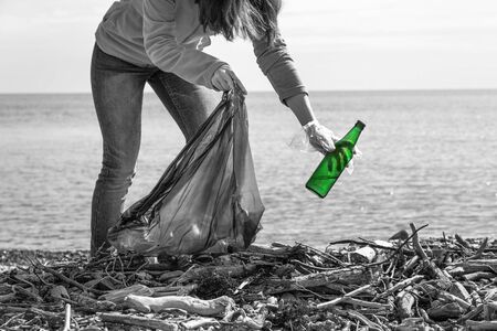 A woman bends down to collect a dirty bottle. Cleaning and environmental protection. Black-and-white...
