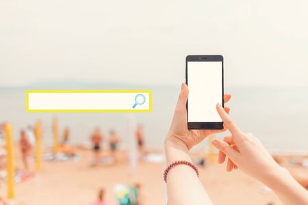 Mock up. Female hands holding the phone on the background of the beach and the rest of people. Copy...
