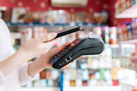 A woman holds a payment terminal and pays for a purchase using a smartphone.On the phone...
