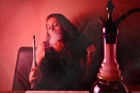 Woman Smoking hookah and posing for the camera. Around circles of steam and smoke. Red tint and...