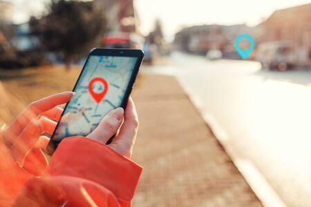 Concept of Internet maps and navigation. Female hands hold smartphone with maps app, and marked location icon, red and blue destination icon.の写真素材
