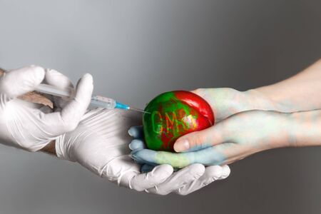 Man wearing medical gloves introduces a chemical into the fruit of the peach lying in the hands of...