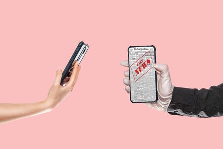 A man in a black shirt and medical gloves holds a smartphone with fake news. On the left, a woman's hand substitutes a smartphone. Pink background.The concept of disinformation and false news on the Internet.の写真素材
