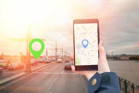 A woman's hand in a jacket holds a smartphone with an online map app. In the background is a blurred...