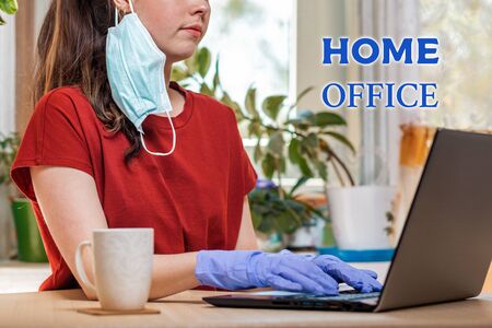 Freelance.A young beautiful Caucasian woman in a medical mask and gloves, typing on a laptop.Home office. Close up.Concept of quarantine, self-isolation and coronovirus.の写真素材