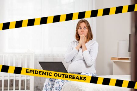 Do not cross.Barrier tape - quarantine, isolation.A pregnant woman is sitting on the bed with a laptop on her lap, with a shocked face.The concept of coronavirus and quarantine. Copy space.の写真素材