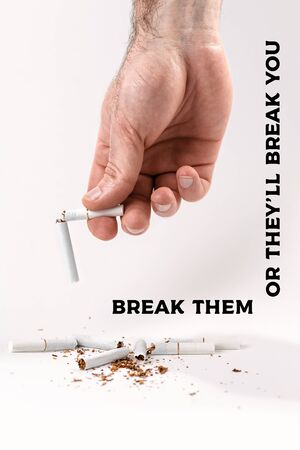 The concept of nicotine addiction and anti-Smoking. A man's hand holds a cigarette broken in half, at the bottom are the fragments of cigarettes. White background. Vertical. Copy space. The inscription Break them or they'll break you'.の写真素材