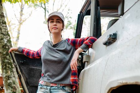 A portrait young Caucasian woman poses next to a jeep. Trees in the background. Close up. Concept of car travel and tourism.の写真素材