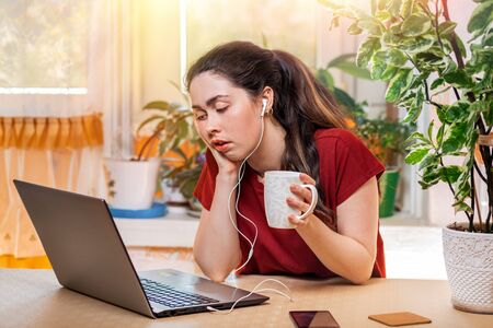 A young beautiful Caucasian woman,with a bored look, holds a mug in her hands,and sleepily looks at...