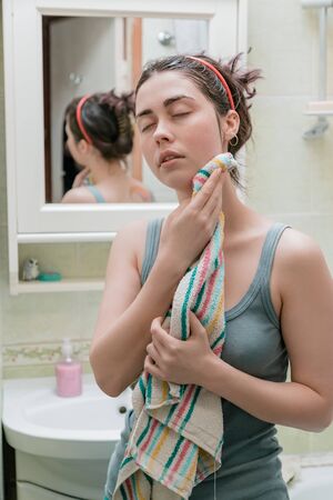 cute girl wipes her face with a towel after water treatments standing in front of a mirror.の写真素材