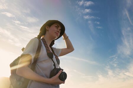 girl tourist with a backpack and a camera on the background of blue sky and sunset ,photos from the...