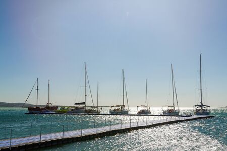 Several yachts in a row are parked at the pier. Blue sky and sea in the background. Skyline.