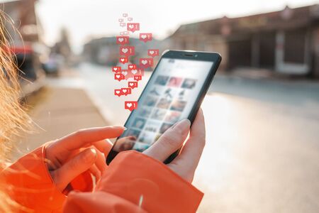 Concept of social networks. Female hands hold a smartphone and press something in it. Icons of likes...
