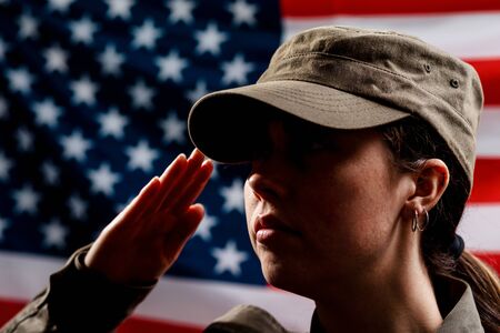Memorial day. A portrait of female soldier in uniform salutes against the background of the American flag. Side view. The concept of the American national holidays and patriotism.の写真素材