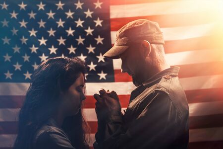 Independence day, memorial Day. A soldier holds a woman's hands. Couple on the background of the American flag. Side view. Concept of American national holidays and patriotism.の写真素材